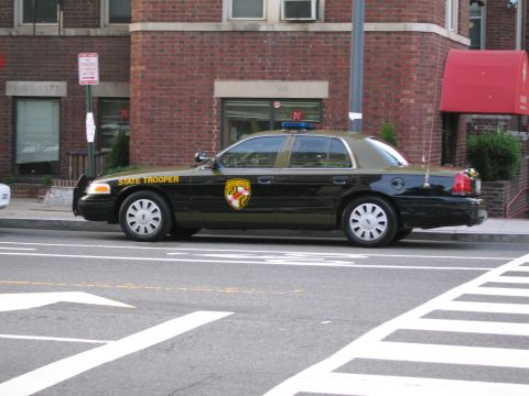 1991 Ford LTD Crown Victoria - black and tan Maryland State Trooper Ford sedan parked along a curb in front of a red brick building.