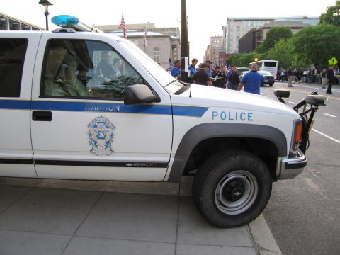1991 Ford LTD Crown Victoria - Close side view of a white and blue Aviation Police Chevrolet 2500 pickup with a crest, parked on a city street.
