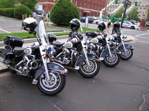 1991 Ford LTD Crown Victoria - row of four black police motorcycles with white windshields and numbered fairings parked on pavement near brick buildings.