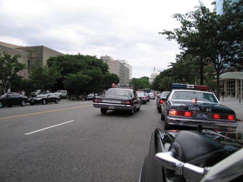 1991 Ford LTD Crown Victoria - line of police cars travels down a tree-lined city avenue toward the U.S. Capitol dome on an overcast day.