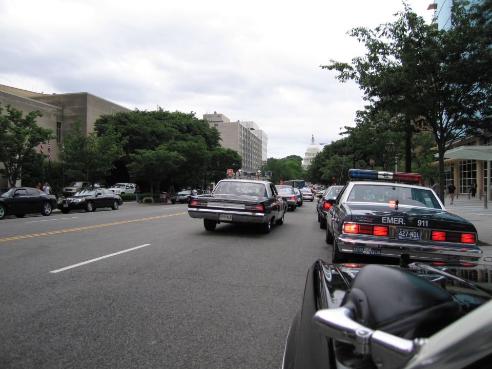 Police cars driving a city avenue toward the U.S. Capitol dome under cloudy sky