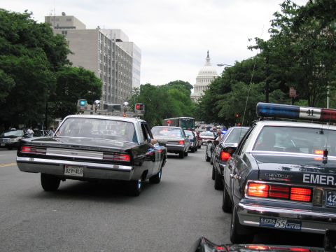 1991 Ford LTD Crown Victoria - black vintage muscle car and modern patrol cars share a city street with the U.S. Capitol dome rising in the background.