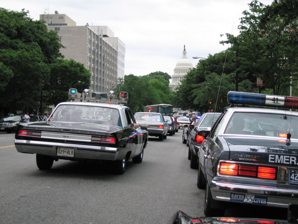 Vintage black muscle car and patrol cars on a city street with the U.S. Capitol behind