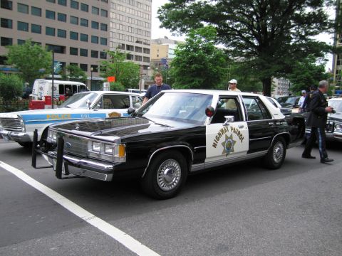 1991 Ford LTD Crown Victoria - black-and-white Ford full-size sedan lettered HIGHWAY PATROL with a star door shield sits on a city street as people stand nearby.