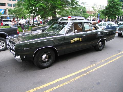 1991 Ford LTD Crown Victoria - dark green vintage Plymouth four-door police sedan with a gold POLICE shield on the door parked along a city street.