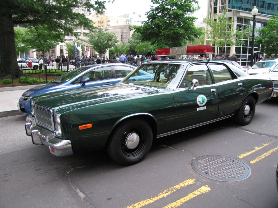 Dark green vintage Plymouth police sedan with round door decal parked at a city curb