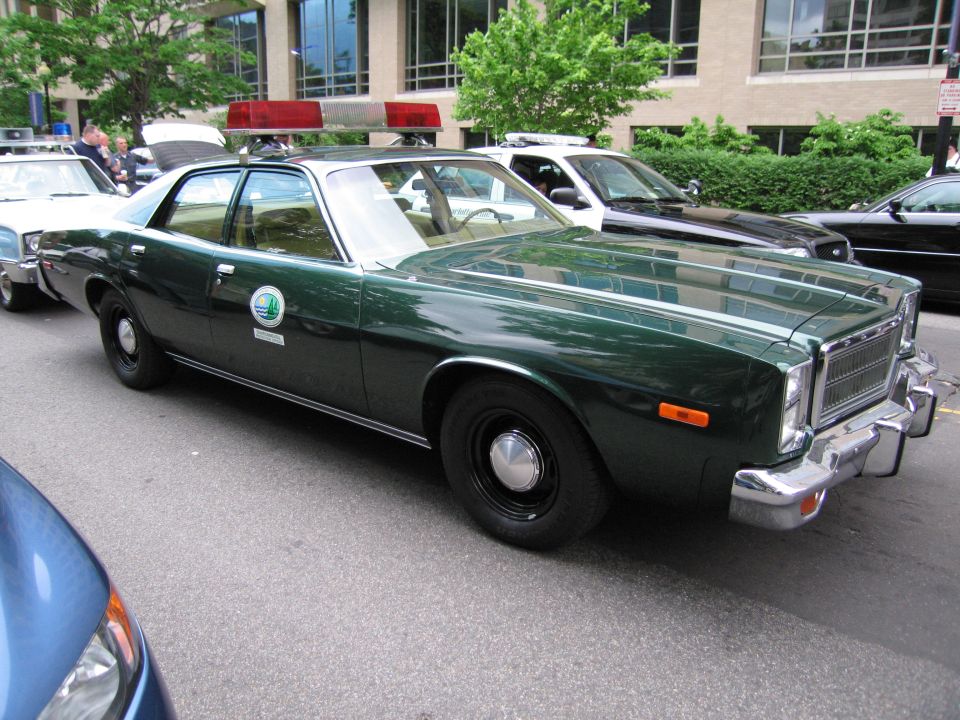 Dark green vintage Plymouth police sedan with red light bar and round door decal at curb