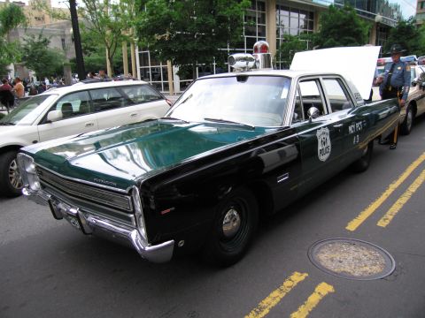 1991 Ford LTD Crown Victoria - green-and-black vintage Plymouth four-door sedan marked POLICE with NYC precinct lettering and a roof light parked on a city street.