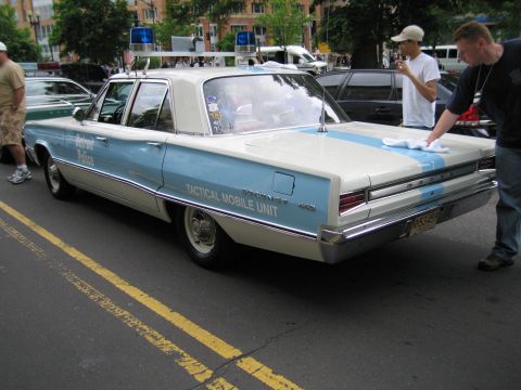 1991 Ford LTD Crown Victoria - man polishes the trunk of a blue-and-white vintage Dodge sedan lettered Detroit Police TACTICAL MOBILE UNIT on a city street.