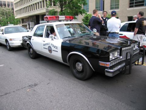 1991 Ford LTD Crown Victoria - black-and-white Jaffrey Police sedan with roof light bar and push bumper parked on a downtown street beside another cruiser.