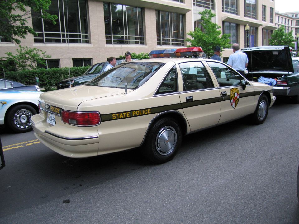 Tan State Police sedan rear view with shield decal on street