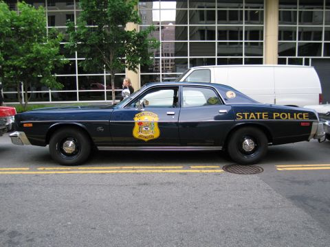 1991 Ford LTD Crown Victoria - Driver-side profile of a navy State Police sedan with gold State Police lettering and a shield decal on the door.