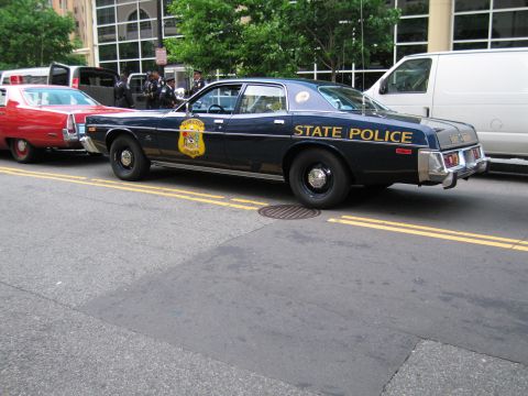 1991 Ford LTD Crown Victoria - Rear quarter view of a navy State Police sedan with gold State Police lettering, parked behind a red car.