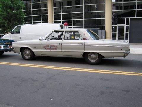 1991 Ford LTD Crown Victoria - Side profile of a cream Police Reserve Monroe County sedan with a red roof beacon, parked along a yellow-lined street.
