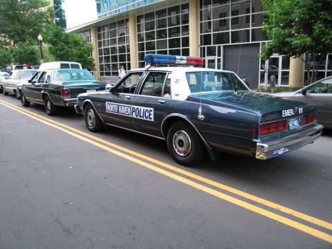 1991 Ford LTD Crown Victoria - Rear quarter view of a dark green North Haven Police sedan with roof light bar, parked behind another sedan.