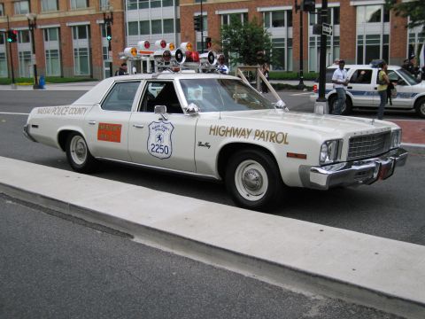 1991 Ford LTD Crown Victoria - cream Nassau County Highway Patrol sedan with multiple roof-mounted lights and speakers, parked at a city curb.