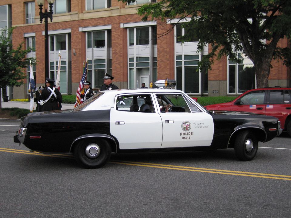 Black and white LAPD-style police sedan in parade with color guard