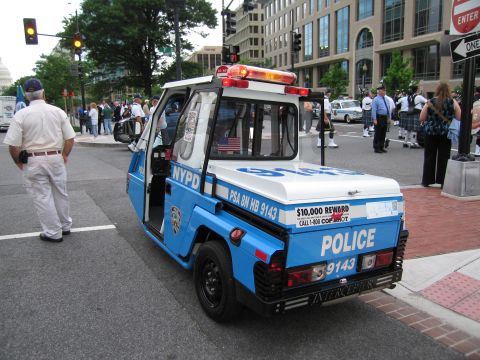 1991 Ford LTD Crown Victoria - blue and white three-wheeled NYPD parking-enforcement scooter marked POLICE 9143 sits on a city street as an officer stands nearby.