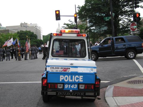 1991 Ford LTD Crown Victoria - Rear view of a blue NYPD POLICE 9143 three-wheeled scooter facing a street procession with the U.S. Capitol dome in the distance.