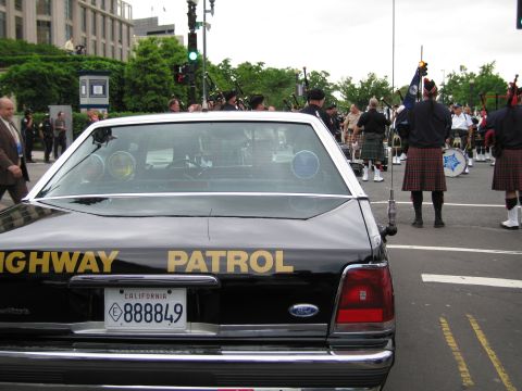1991 Ford LTD Crown Victoria - rear of a black-and-white California Highway Patrol Ford sedan with plate 888849 sits near kilted bagpipers in a street procession.