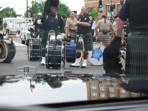 1991 Ford LTD Crown Victoria - Kilted pipe-band members in tartan, including a drum lettered Chicago Police, gather on a street seen over a car's reflective hood.