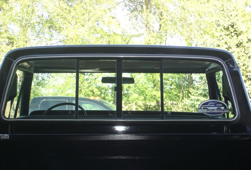 View through a truck's rear window showing another vehicle and trees outside
