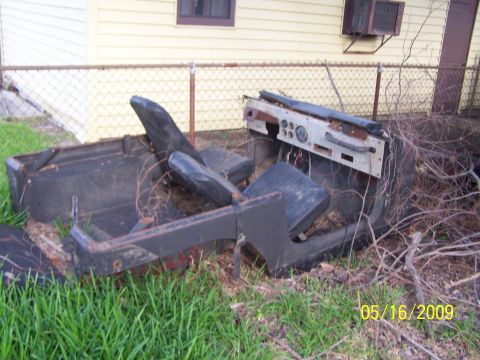 1982 Ford Bronco - The interior of an abandoned vehicle, showing worn seats and a damaged dashboard, overgrown with weeds and branches.