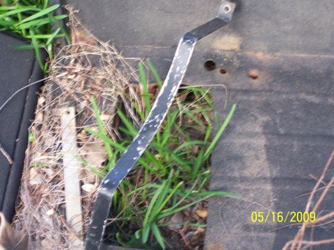 1982 Ford Bronco - A metal bracket is seen on a dark surface with grass and debris, dated 05/16/2009.