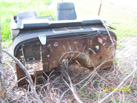 1982 Ford Bronco - This heavily rusted vehicle front end, including seats, sits abandoned outdoors amongst weeds and branches.