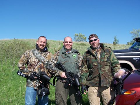 1986 Ford Bronco - Three men pose with paintball guns in a grassy field, with vehicles in the background.