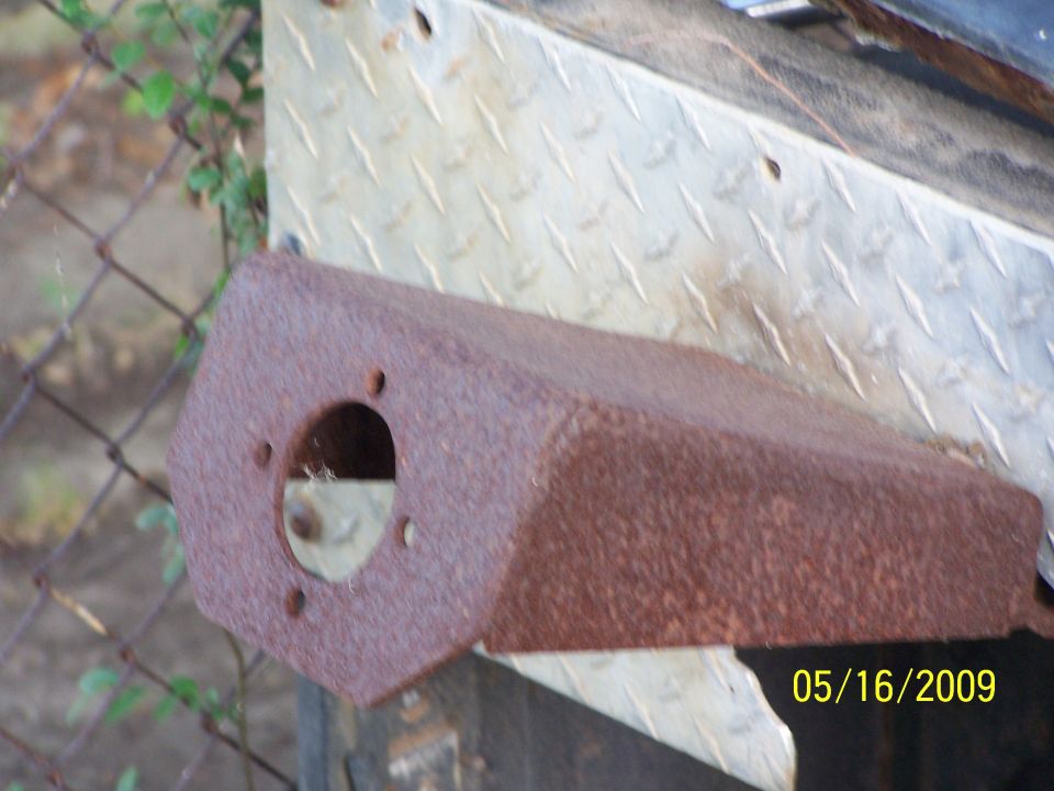 Rusted metal part with a circular opening and four bolt holes, mounted on diamond plate