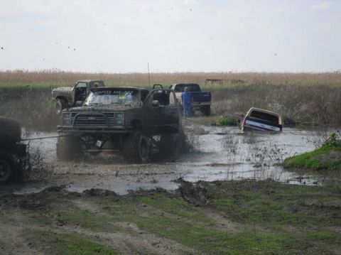 1990 Ford Bronco - Multiple trucks are stuck in the mud during an off-road event.