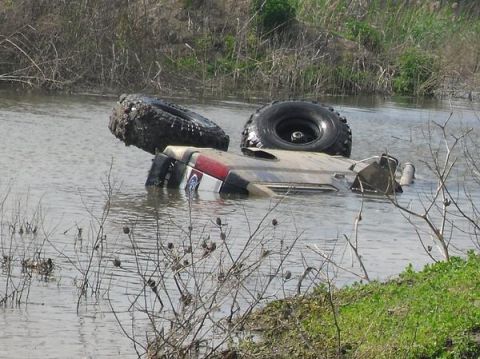 1990 Ford Bronco - An off-road vehicle is submerged in shallow water, with its tires visible above the surface.