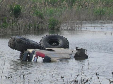 1990 Ford Bronco - A submerged 1990 Ford Bronco lies upside down in a body of water, with its tires sticking out.