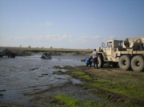 1990 Ford Bronco - A tow truck attempts to rescue vehicles stuck in a muddy body of water.