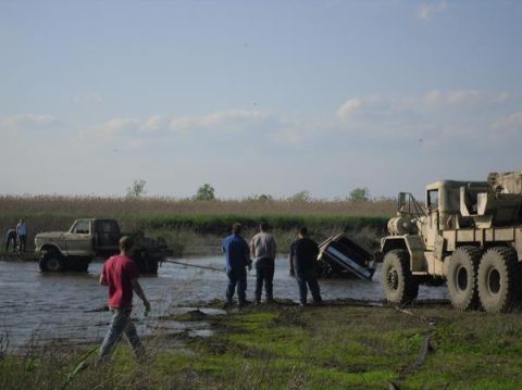 1990 Ford Bronco - A group of people are attempting to free vehicles stuck in a muddy, watery area.