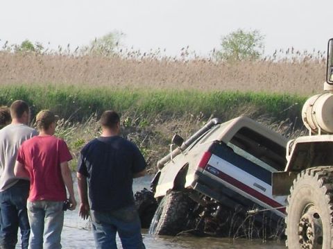1990 Ford Bronco - A Ford Bronco is stuck in the mud, with a large truck attempting to pull it out.