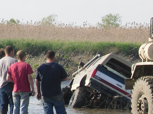 Ford Bronco stuck in mud, being pulled by a large truck. Off-road tires, snorkel visible