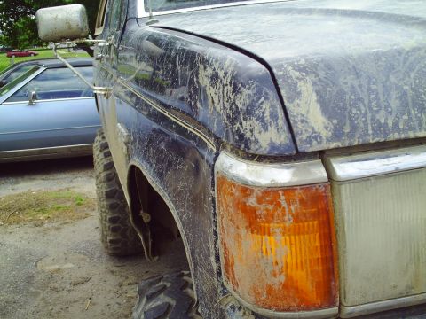 1990 Ford Bronco - A close-up view of a dirty truck's front corner, with another vehicle visible in the background.
