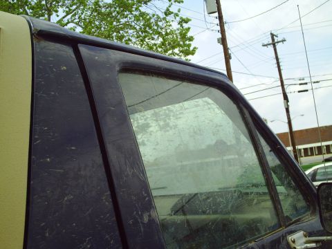 1990 Ford Bronco - A dirty dark blue SUV door and window are visible, with a tan roof section on the left side.