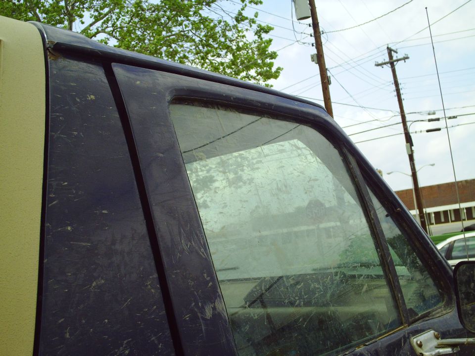 Dark blue SUV door and window covered in dirt, with a tan roof visible on the left