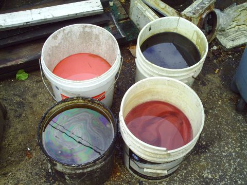 1990 Ford Bronco - Various liquids are contained in buckets, some showing iridescent sheens and others a deep red or black hue.
