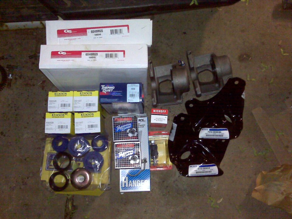 Collection of vehicle parts including boxes labeled GS 604RGS, Thermo-Quiet, Performance Suspension, and two black metal brackets with Ford labels