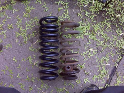 1995 Ford Bronco - A new black coil spring sits next to an old, rusted coil spring on the ground.
