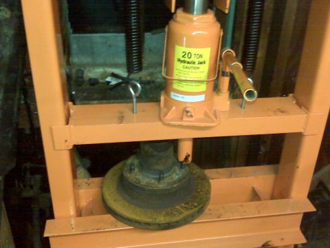 1995 Ford Bronco - A brake rotor is being pressed by a hydraulic jack within an orange metal frame.