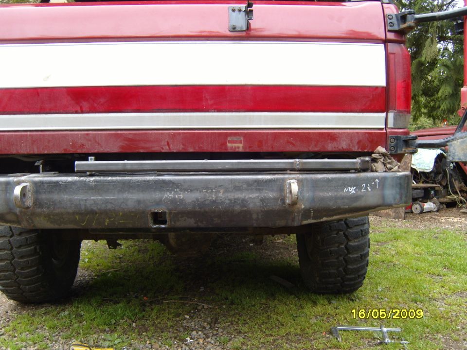 Red truck rear bumper with white stripe, aftermarket metal bumper, visible tires and grass