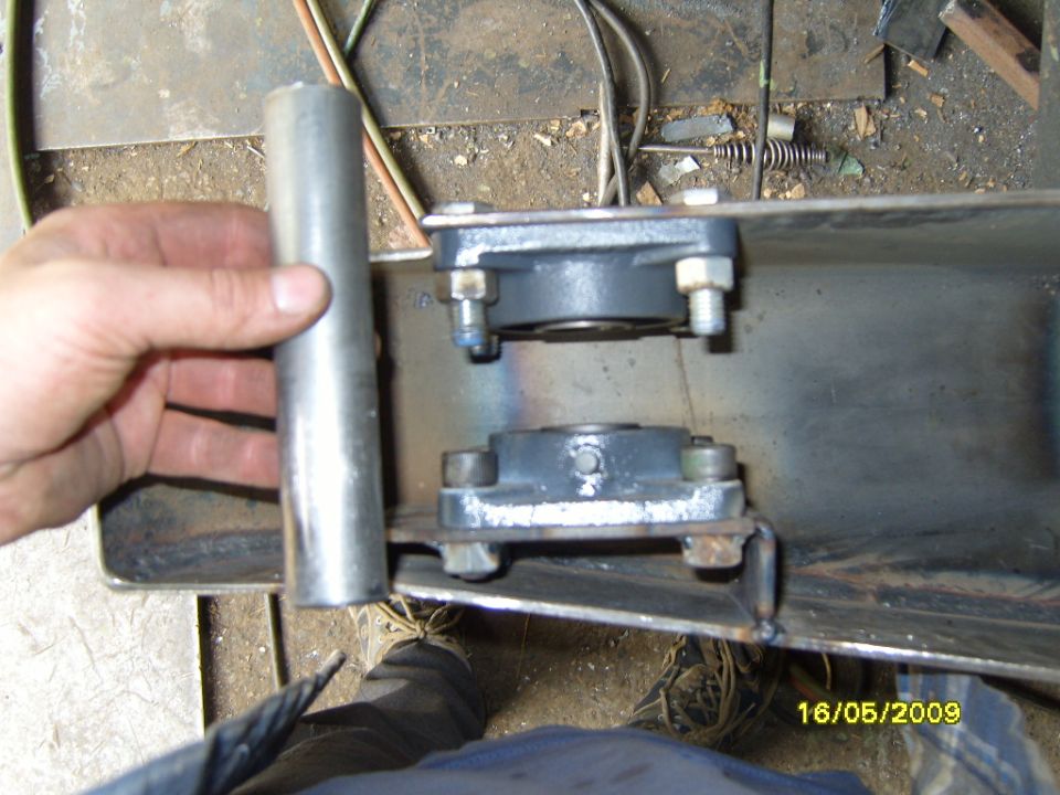 Hand holding metal pipe near two bearing mounts attached to metal frame