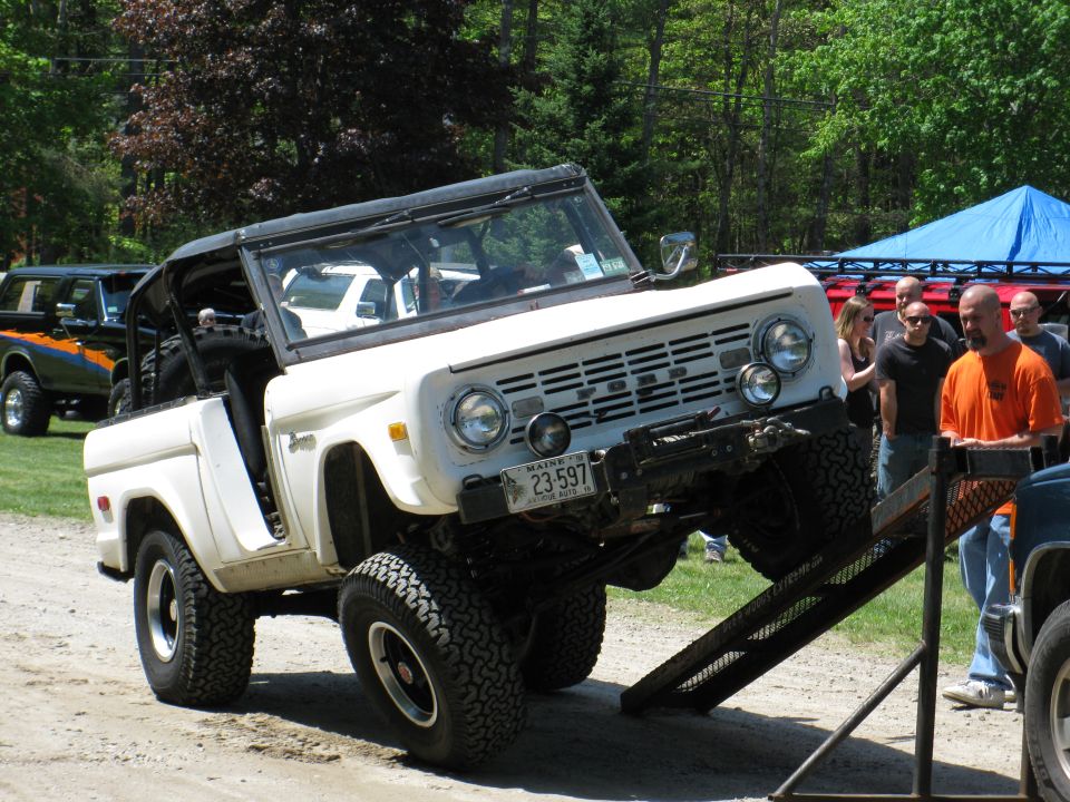 White Ford Bronco driving up a ramp with another Bronco in the background
