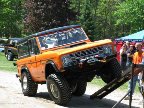 1973 Ford Bronco - Orange 1973 Ford Bronco ascends a ramp, with 'BRONCO' visible on the windshield and another Bronco in the background.