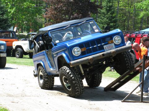1973 Ford Bronco - A blue 1973 Ford Bronco is shown with its front wheels on a ramp, while other vehicles are parked nearby.